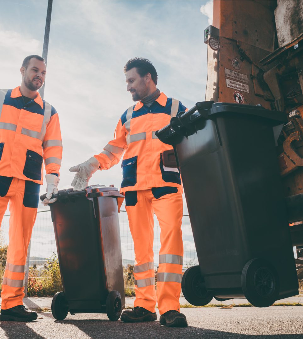 Two men in orange work suits holding trash cans.