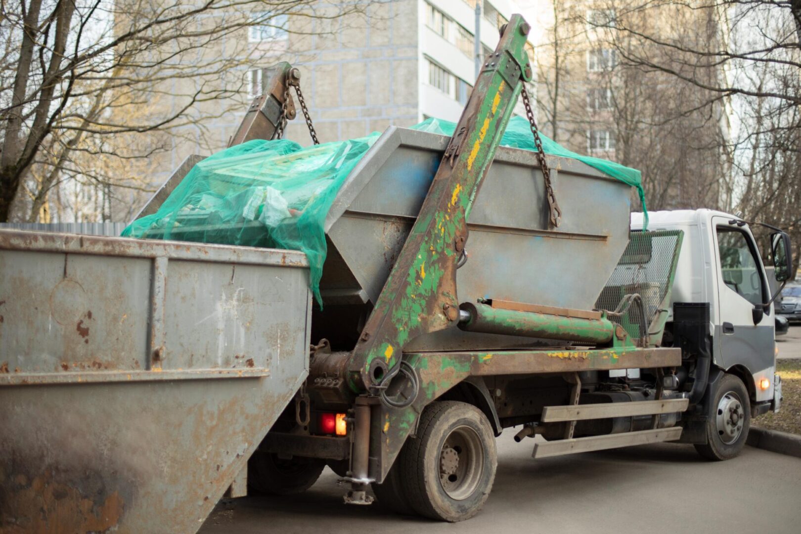 A dumpster being loaded onto the back of a truck.