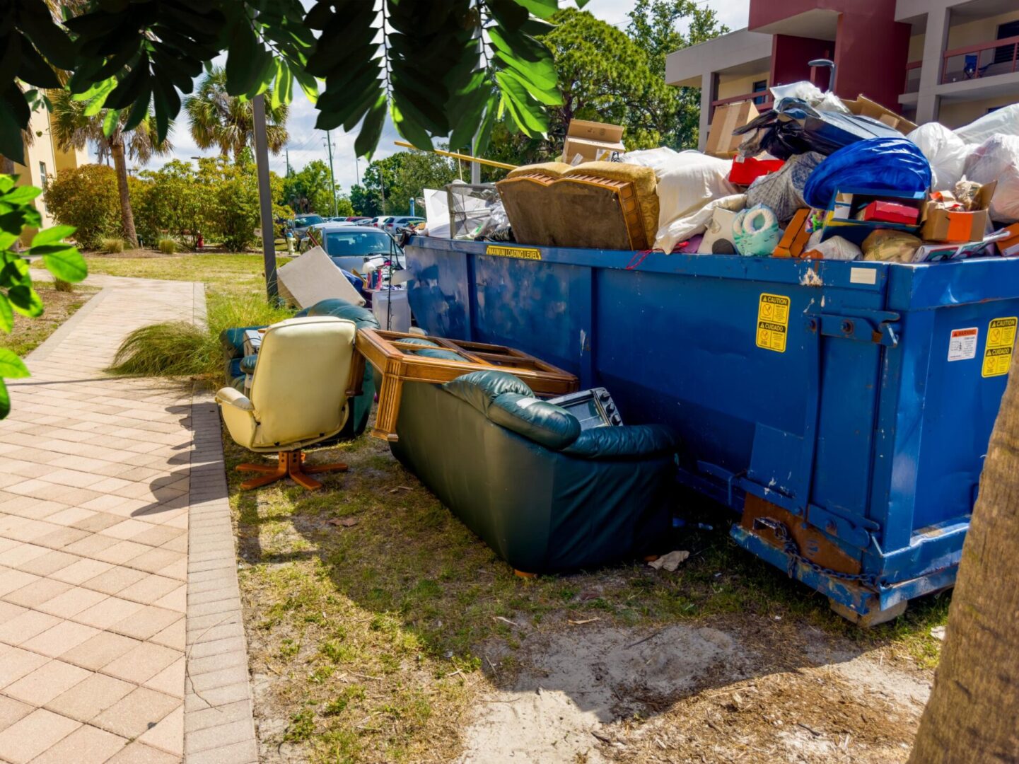 A dumpster full of trash next to a sidewalk.